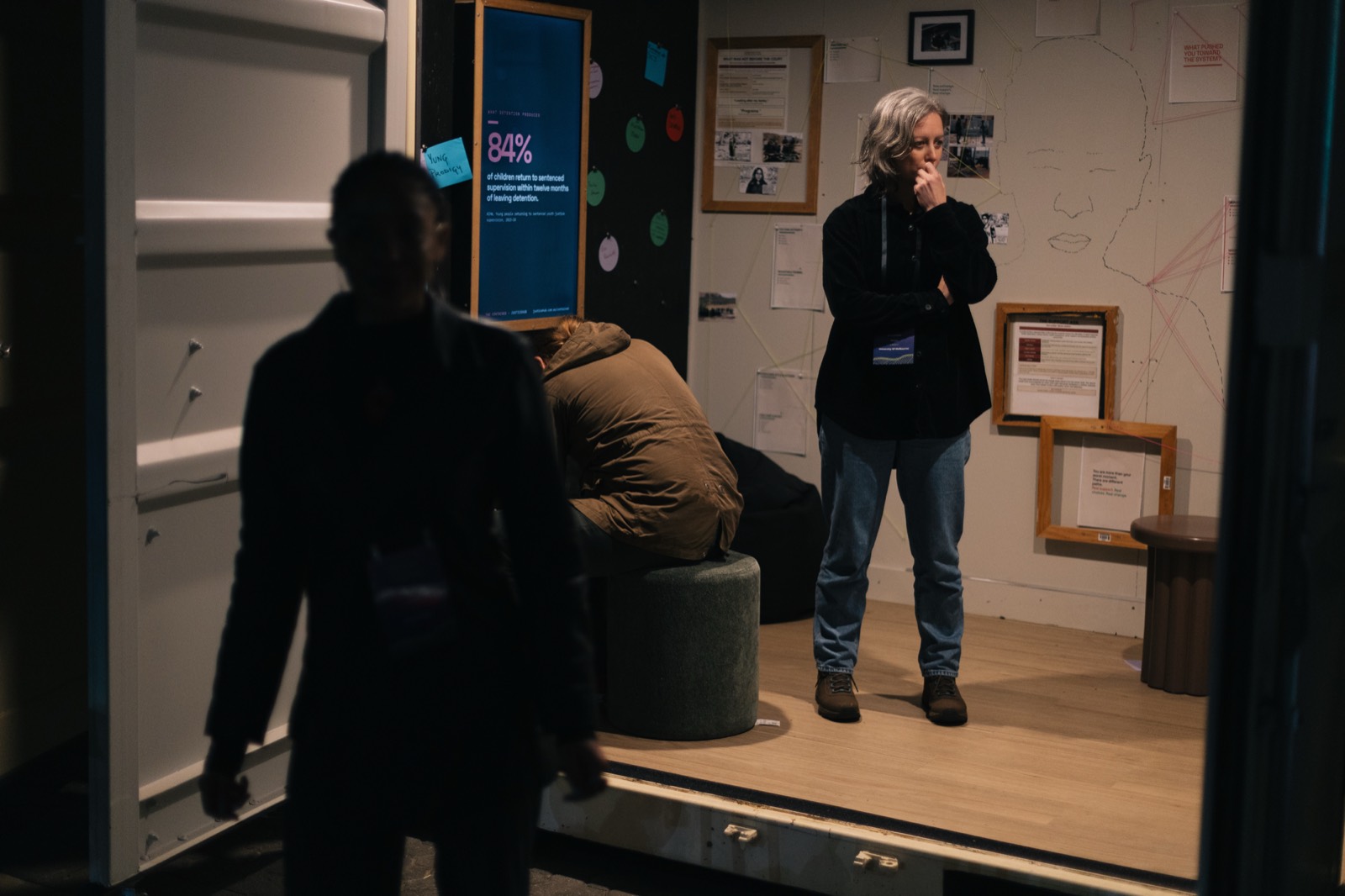 A woman stands alone in the evidence room, hand to her mouth, in front of a screen reading 84% of children return to sentenced supervision within twelve months of leaving detention