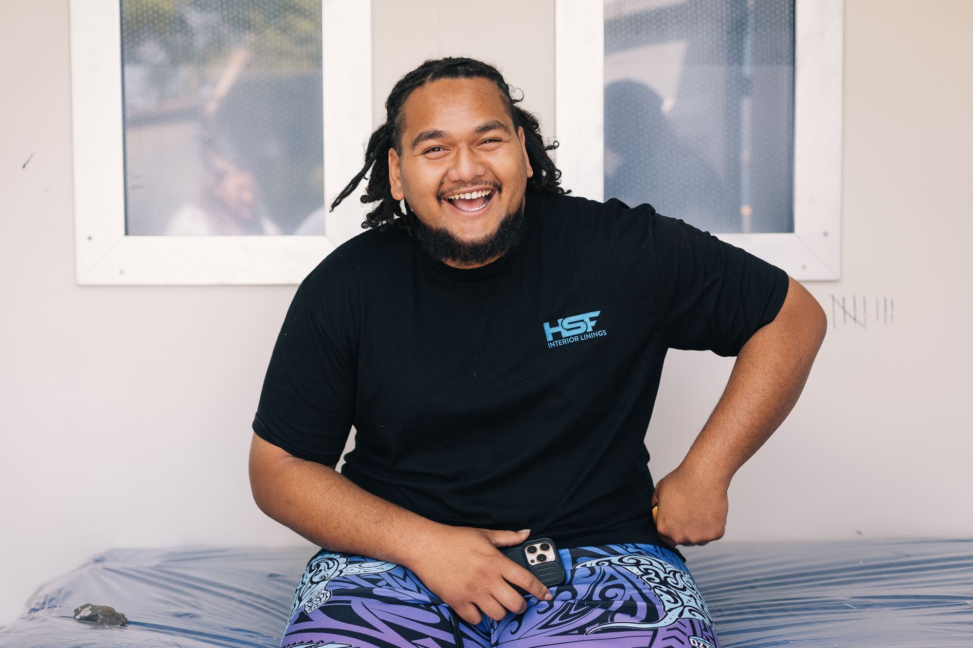 Isaiah laughs, sitting on the plastic-wrapped bed in the CONTAINED cell room, two barred windows behind him