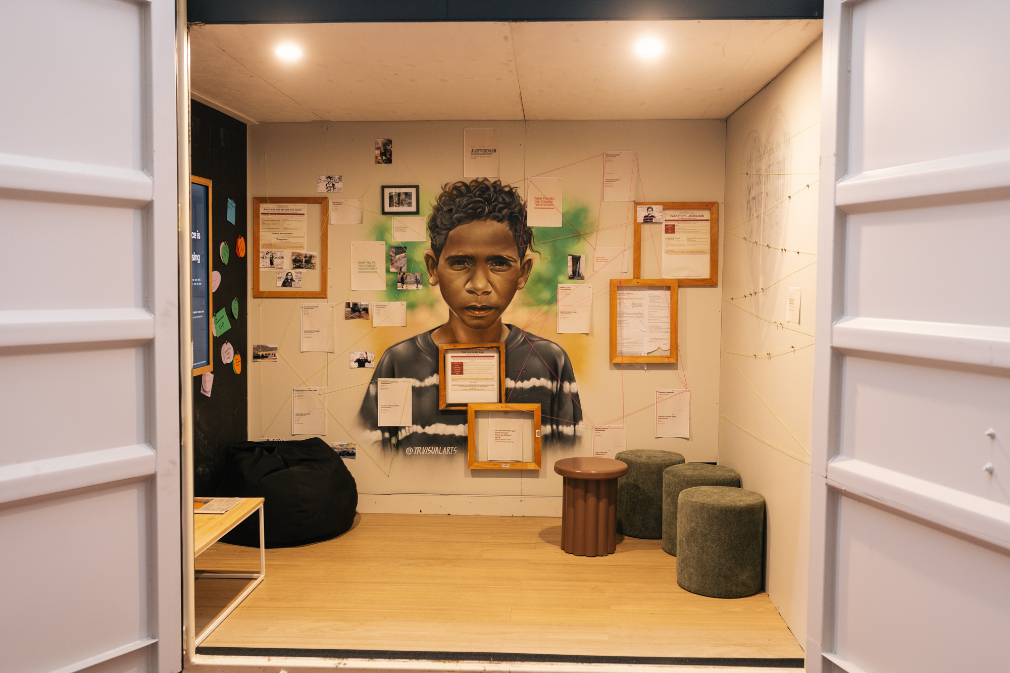 Seen through the open container doors, Thomas Readett’s painted portrait of Jackquann fills the community room wall, surrounded by framed notes and photographs