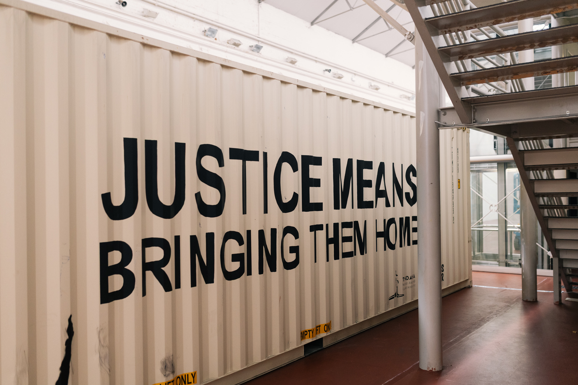 The long side of the shipping container inside Tandanya, painted with the words JUSTICE MEANS BRINGING THEM HOME